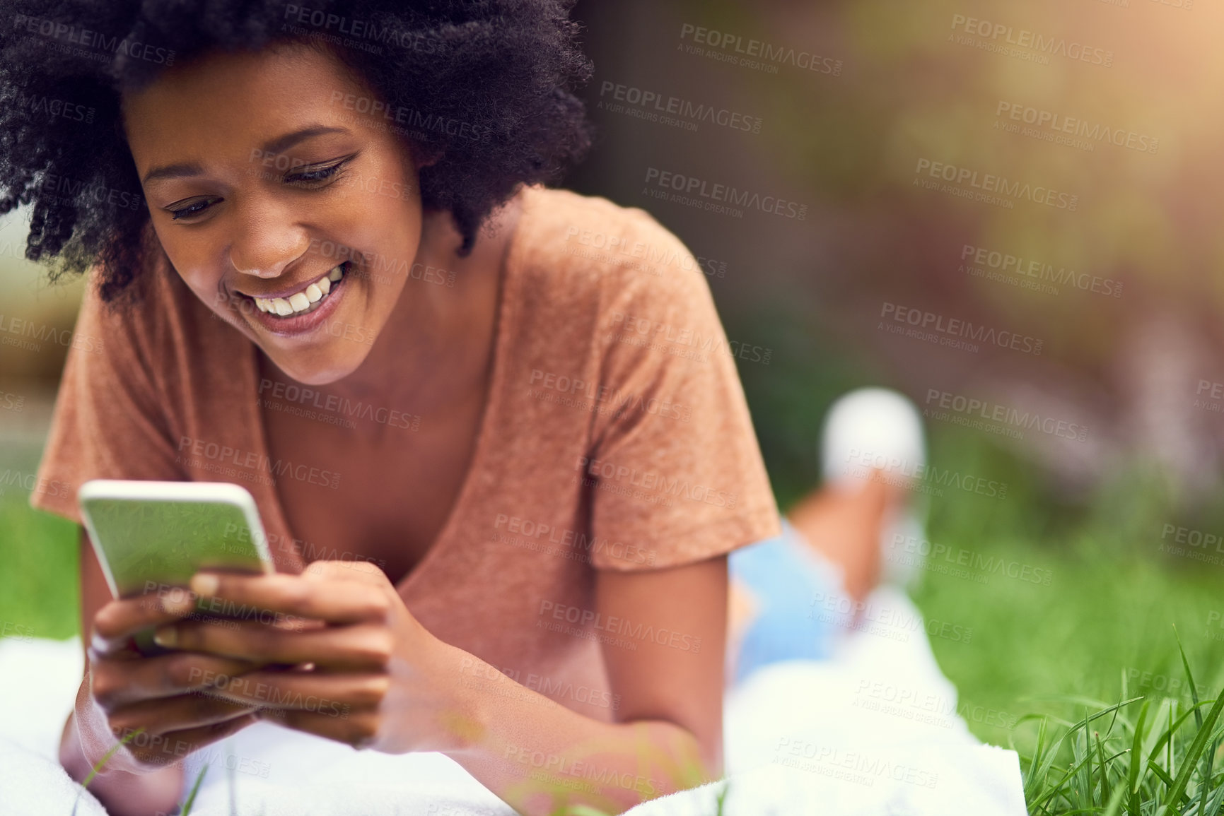 Buy stock photo Shot of a young man texting while relaxing at the park