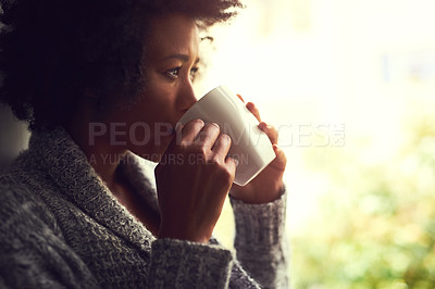 Buy stock photo Shot of a relaxed young woman enjoying a cup of coffee while sitting by a window at home