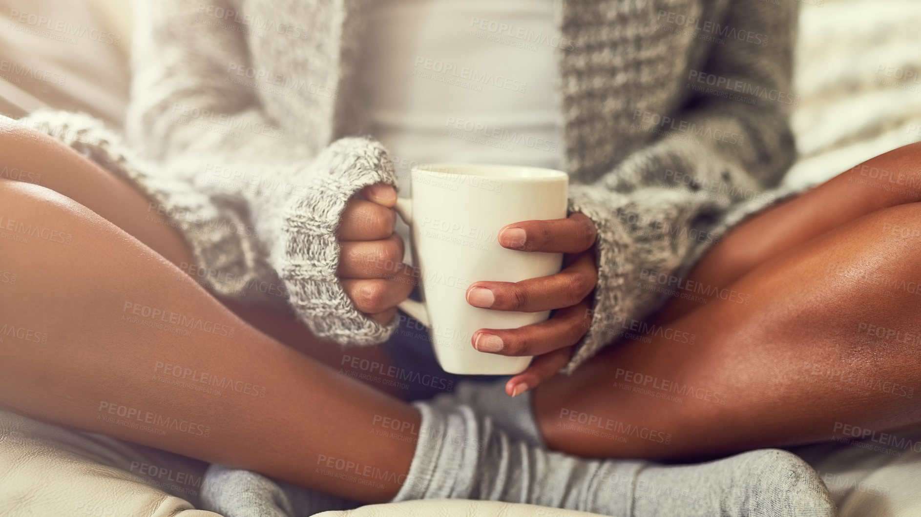 Buy stock photo Shot of an unidentifiable young woman enjoying a cup of coffee while sitting on her couch at home