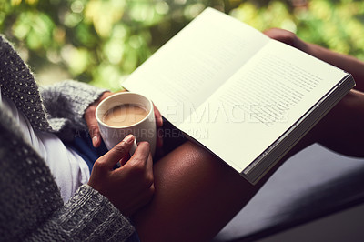 Buy stock photo Shot of an unidentifiable young woman reading a book while enjoying a cup of coffee at home