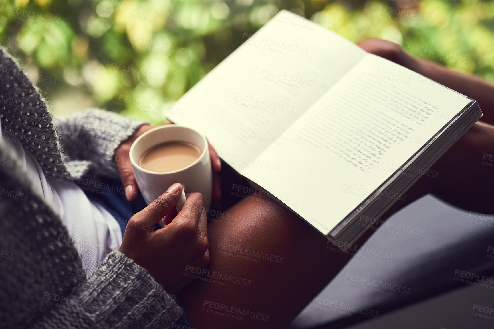 Buy stock photo Shot of an unidentifiable young woman reading a book while enjoying a cup of coffee at home