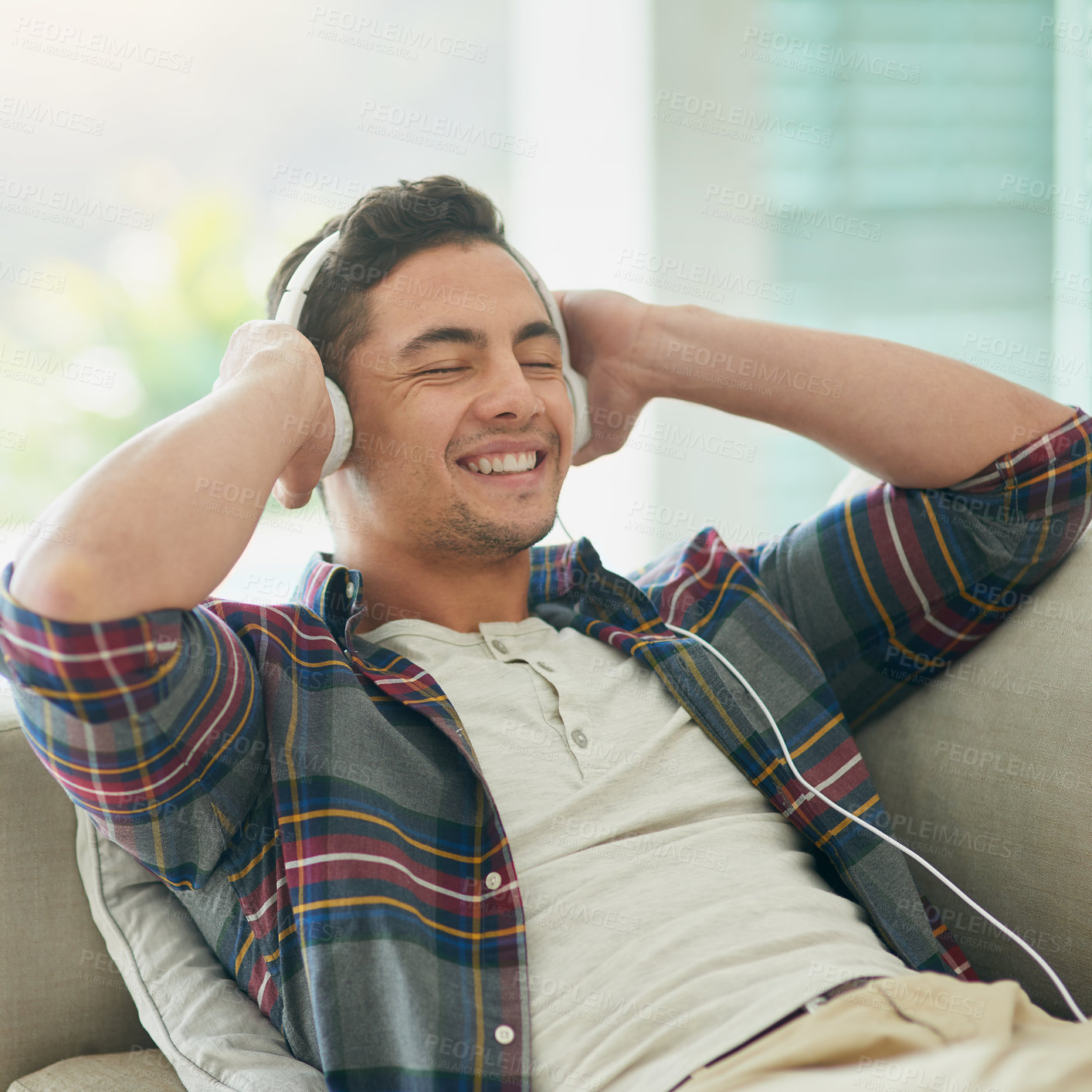 Buy stock photo Shot of a young man relaxing on the sofa and listening to music with headphones at home