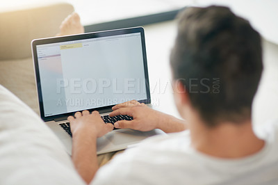 Buy stock photo Rearview shot of a relaxed young man using a laptop on the sofa at home