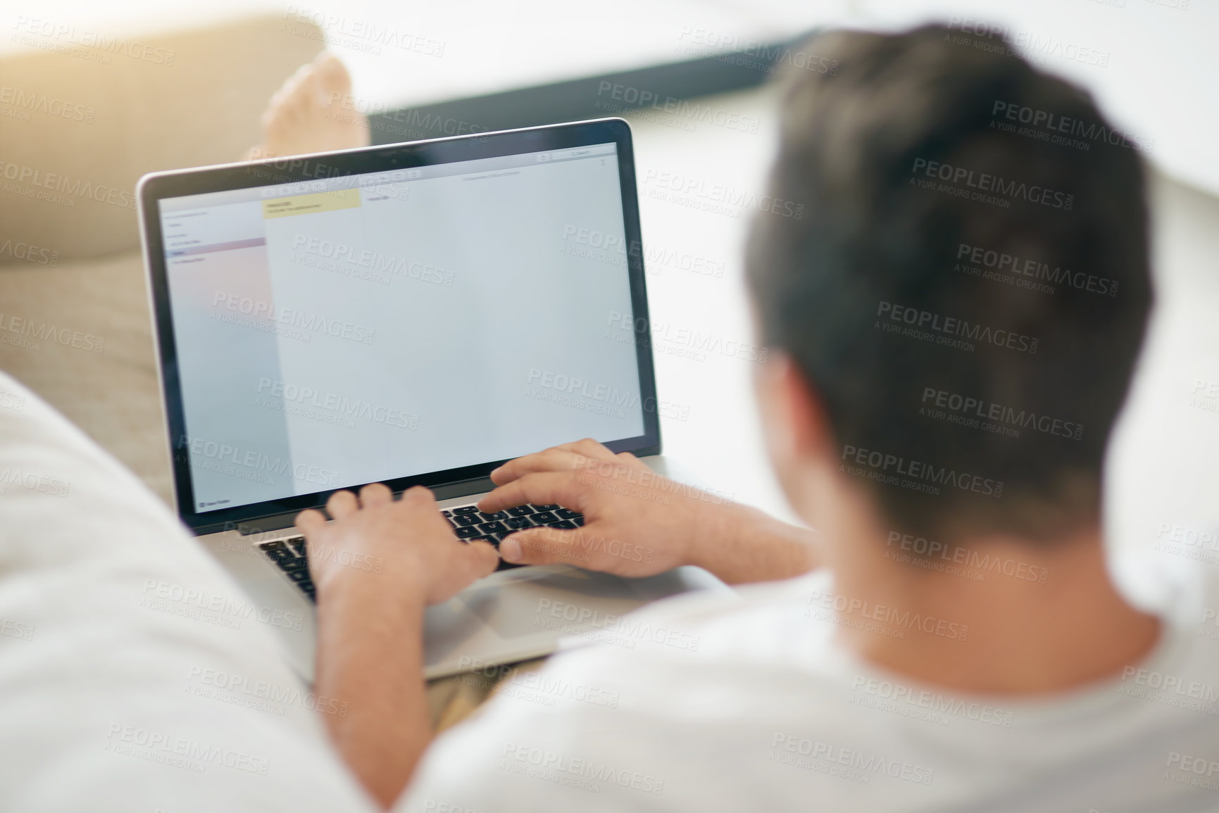Buy stock photo Rearview shot of a relaxed young man using a laptop on the sofa at home