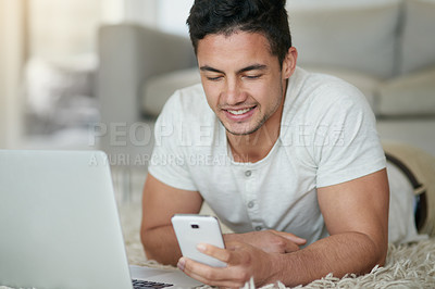 Buy stock photo Shot of a relaxed young man using a phone and laptop on the floor at home