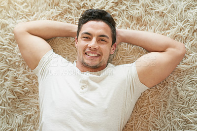 Buy stock photo Portrait of a happy young man relaxing on the carpet at home