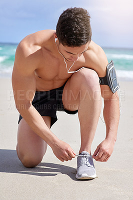 Buy stock photo Shot of a handsome young man tying his laces before his run on the beach