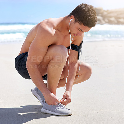 Buy stock photo Shot of a handsome young man tying his laces before his run on the beach