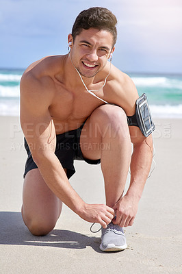 Buy stock photo Portrait of a handsome young man tying his laces before his run on the beach