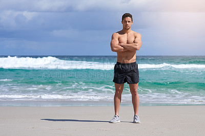 Buy stock photo Portrait of a handsome young man standing with his arms folded on the beach
