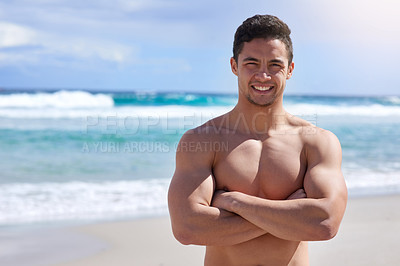 Buy stock photo Portrait of a handsome young man standing with his arms folded on the beach