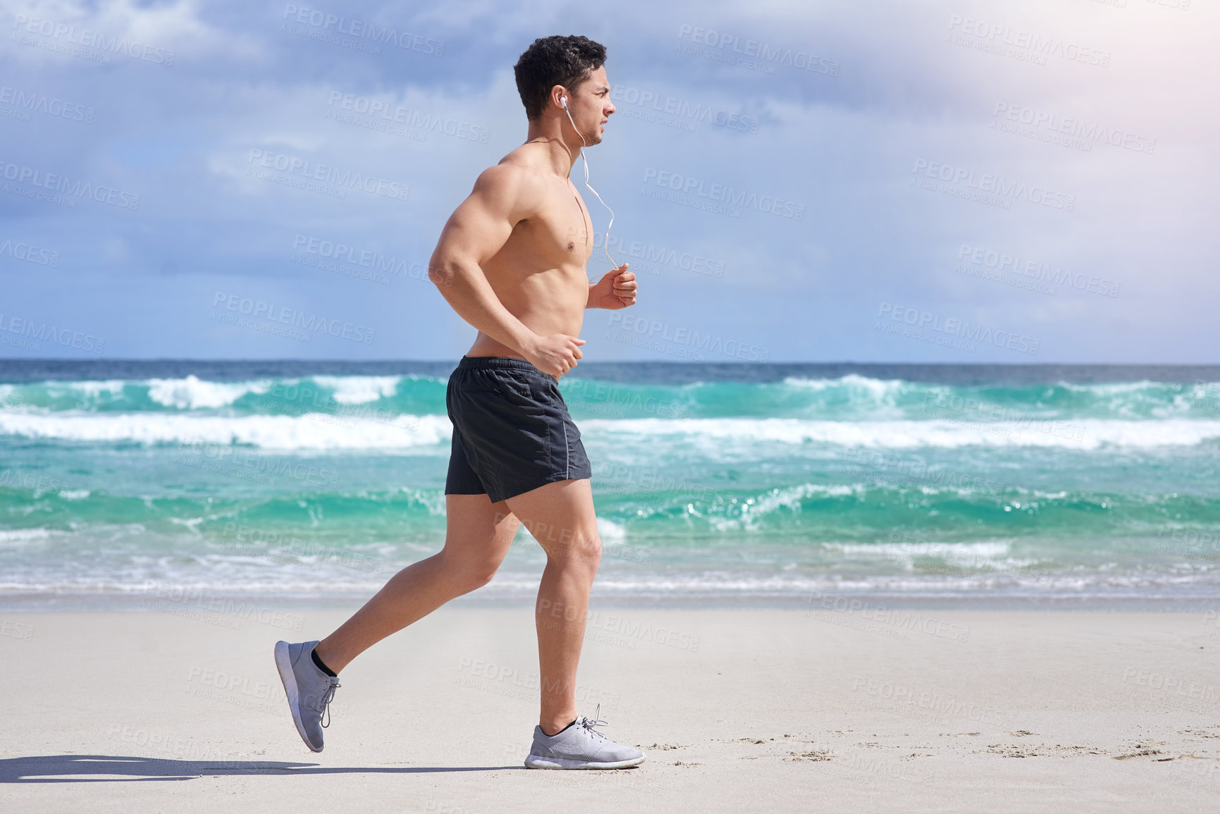 Buy stock photo Shot of a handsome young man jogging on the beach