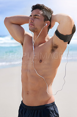 Buy stock photo Shot of a handsome young man standing with his hands behind his back on the beach