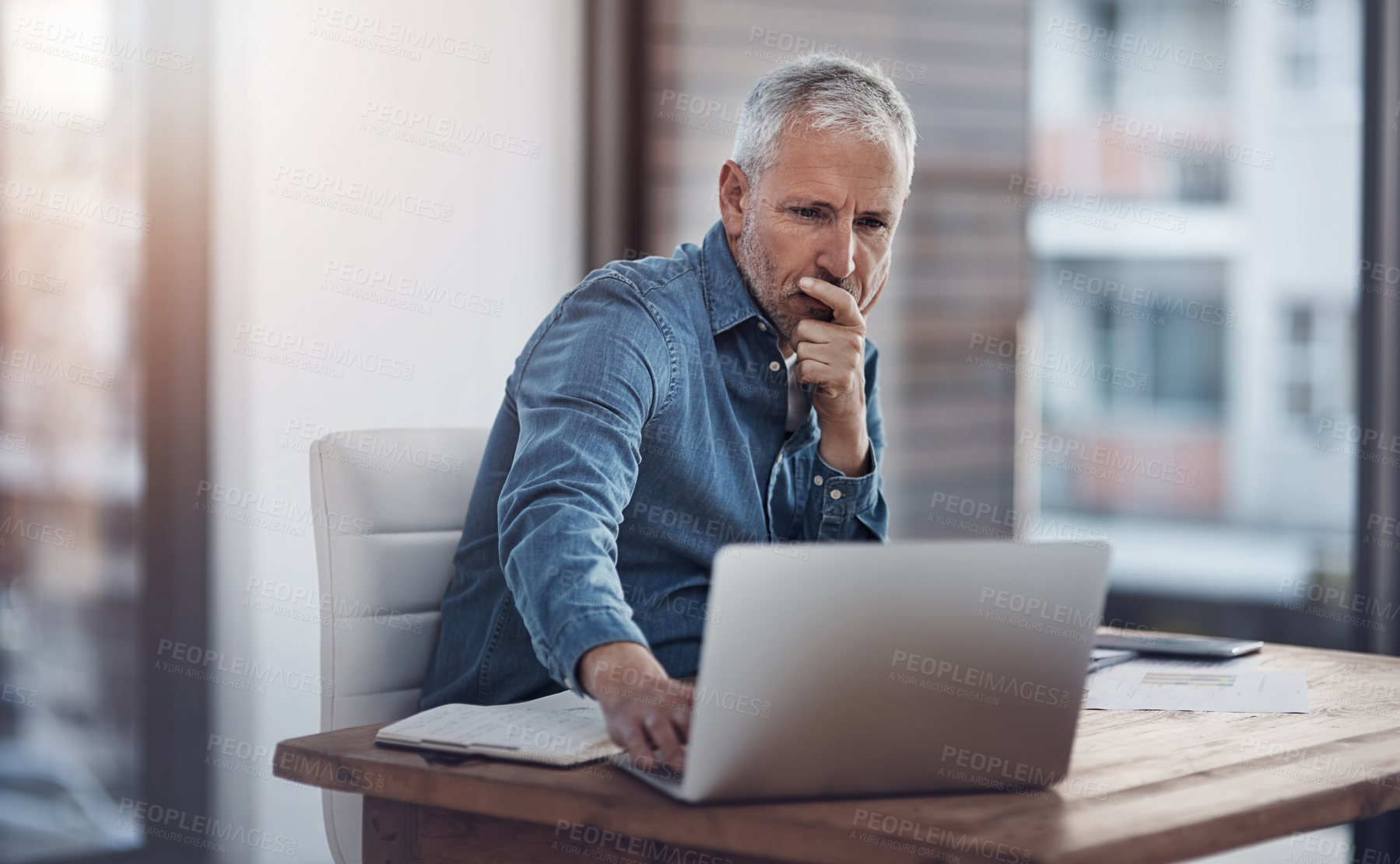 Buy stock photo Cropped shot of a thoughtful mature businessman working on a laptop in an office