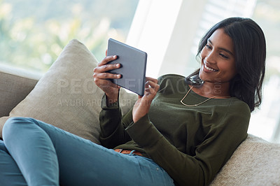 Buy stock photo Shot of an attractive young woman using her tablet while sitting on the sofa at home