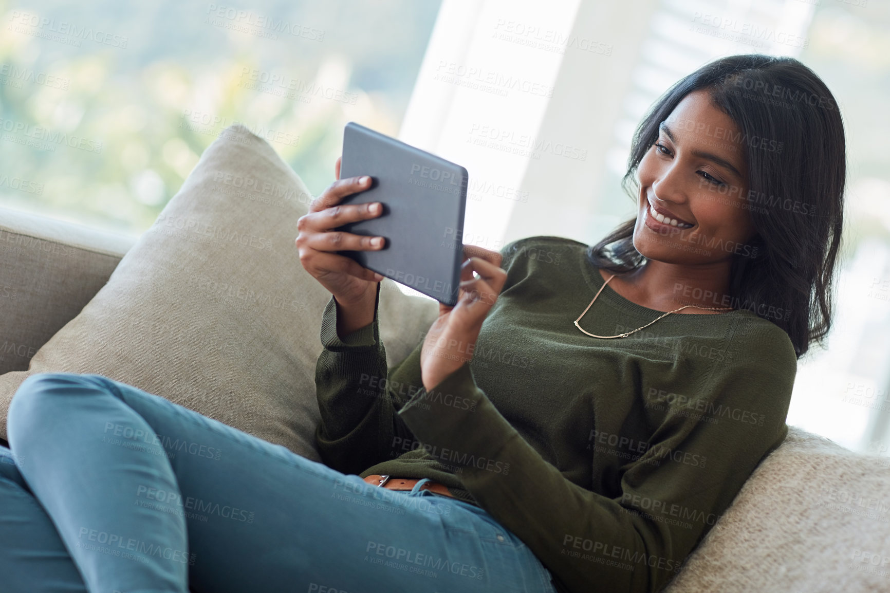 Buy stock photo Shot of an attractive young woman using her tablet while sitting on the sofa at home