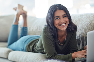 Buy stock photo Portrait of an attractive young woman using her laptop while lying on the sofa at home