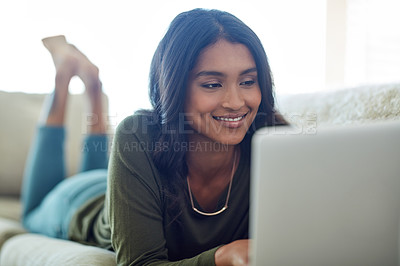 Buy stock photo Shot of an attractive young woman using her laptop while lying on the sofa at home