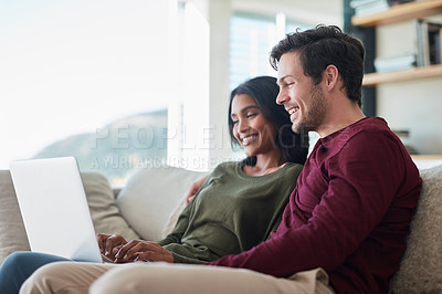 Buy stock photo Shot of an affectionate young couple using their laptop while sitting on the sofa at home