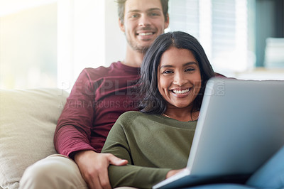 Buy stock photo Portrait of an affectionate young couple using their laptop while sitting on the sofa at home