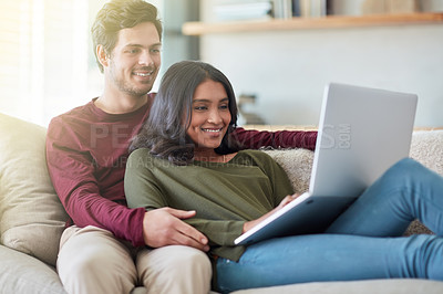 Buy stock photo Shot of an affectionate young couple using their laptop while sitting on the sofa at home