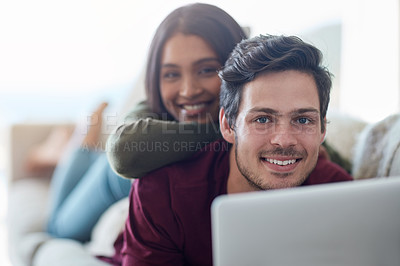 Buy stock photo Portrait of an affectionate young couple using their laptop while lying on the sofa at home