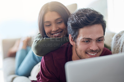 Buy stock photo Shot of an affectionate young couple using their laptop while lying on the sofa at home