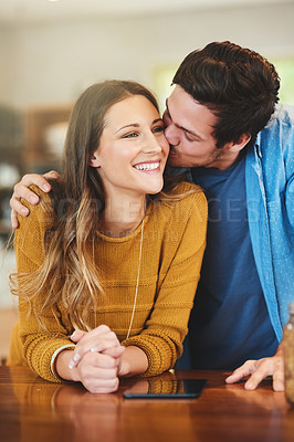 Buy stock photo Shot of an affectionate young man kissing his girlfriend on the cheek in their kitchen