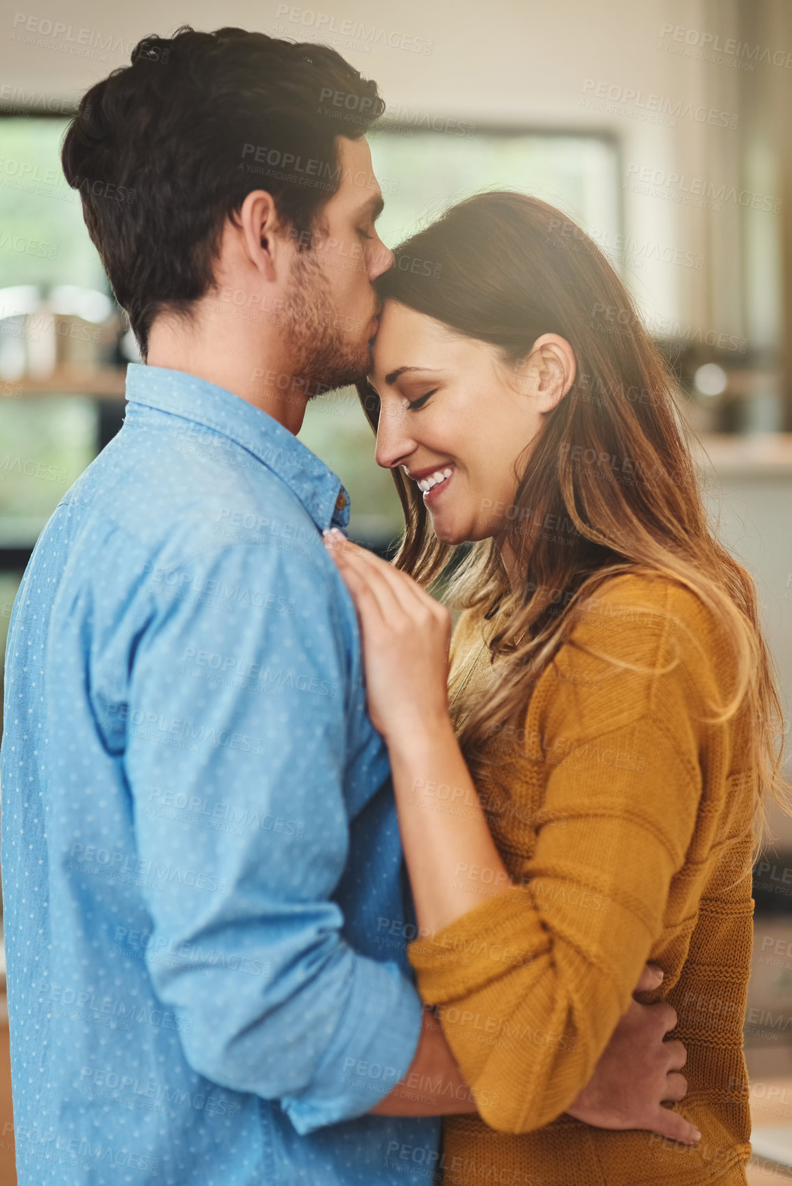 Buy stock photo Shot of an affectionate young man kissing his girlfriend on the forehead in their kitchen