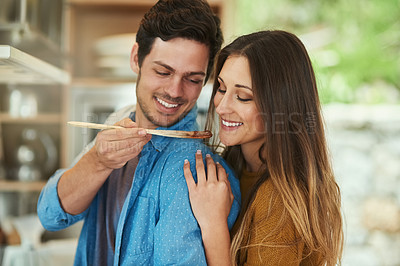 Buy stock photo Shot of a handsome young man giving his girlfriend a taste of what he's cooking
