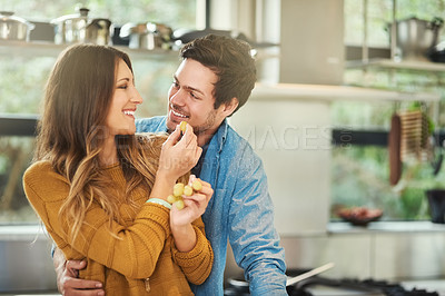 Buy stock photo Shot of an attractive young woman feeding her boyfriend grapes in their kitchen