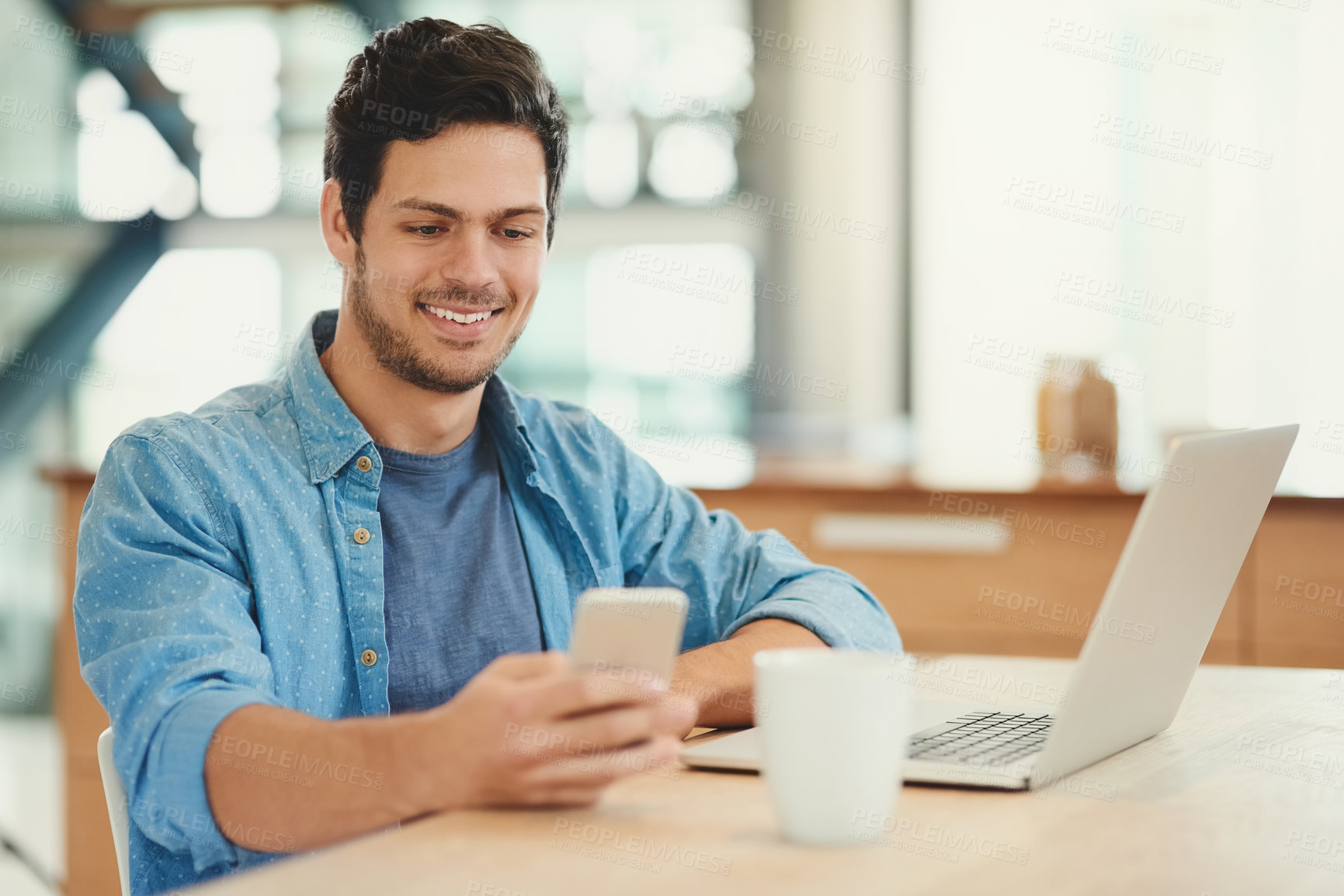 Buy stock photo Shot of a handsome young man using his cellphone and laptop at home