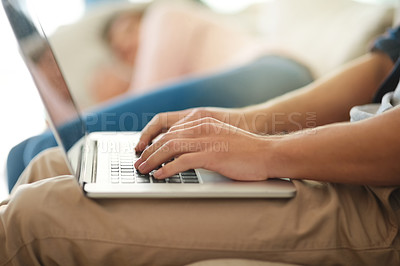 Buy stock photo Shot of an unidentifiable man working on his laptop at home while his wife lies on the couch next to him
