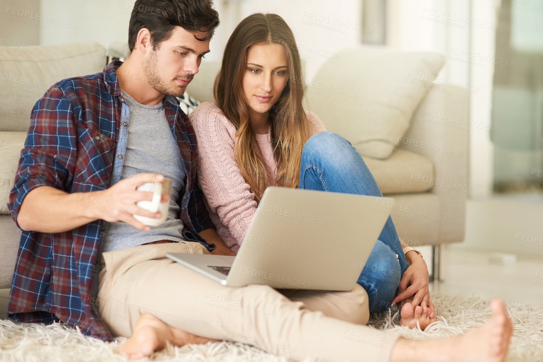 Buy stock photo Shot of a happy young couple using a laptop together while relaxing in their lounge at home