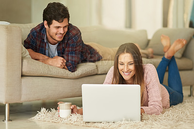Buy stock photo Shot of a happy young couple using a laptop together while relaxing in their lounge at home