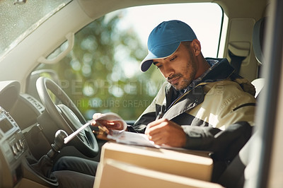 Buy stock photo Shot of a delivery man reading addresses while sitting in a delivery van