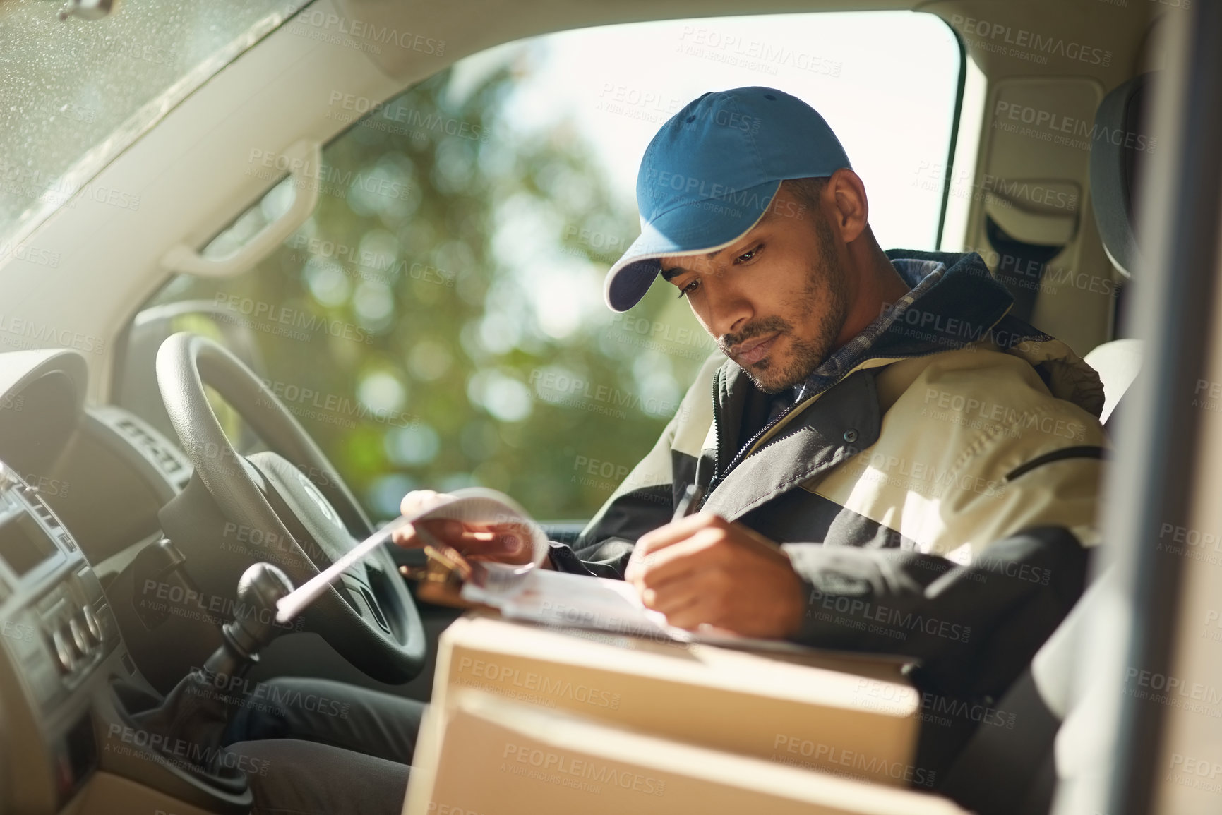 Buy stock photo Shot of a delivery man reading addresses while sitting in a delivery van