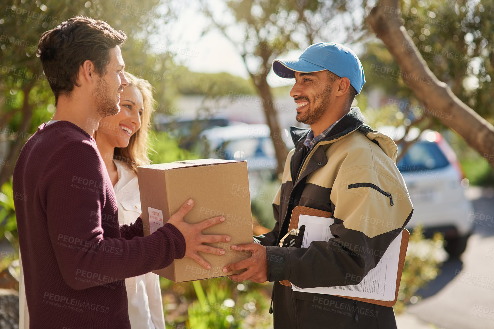 Buy stock photo Shot of a courier delivering a package to a smiling young couple at home