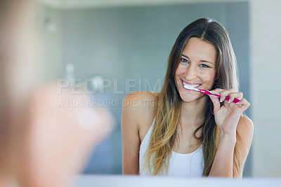 Buy stock photo Portrait of young woman looking in the bathroom mirror while brushing her teeth