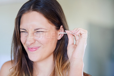 Buy stock photo Shot of young woman pulling a funny face while cleaning her ear with an earbud at home