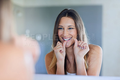 Buy stock photo Shot of a happy young woman using dental floss to clean her teeth at home