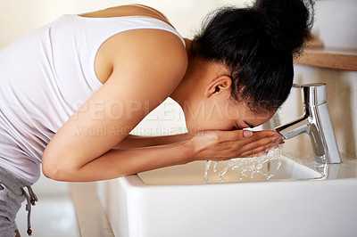 Buy stock photo Shot of a young woman washing her face at the bathroom sink
