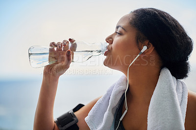 Buy stock photo Cropped shot of a sporty young woman drinking water while out for a run