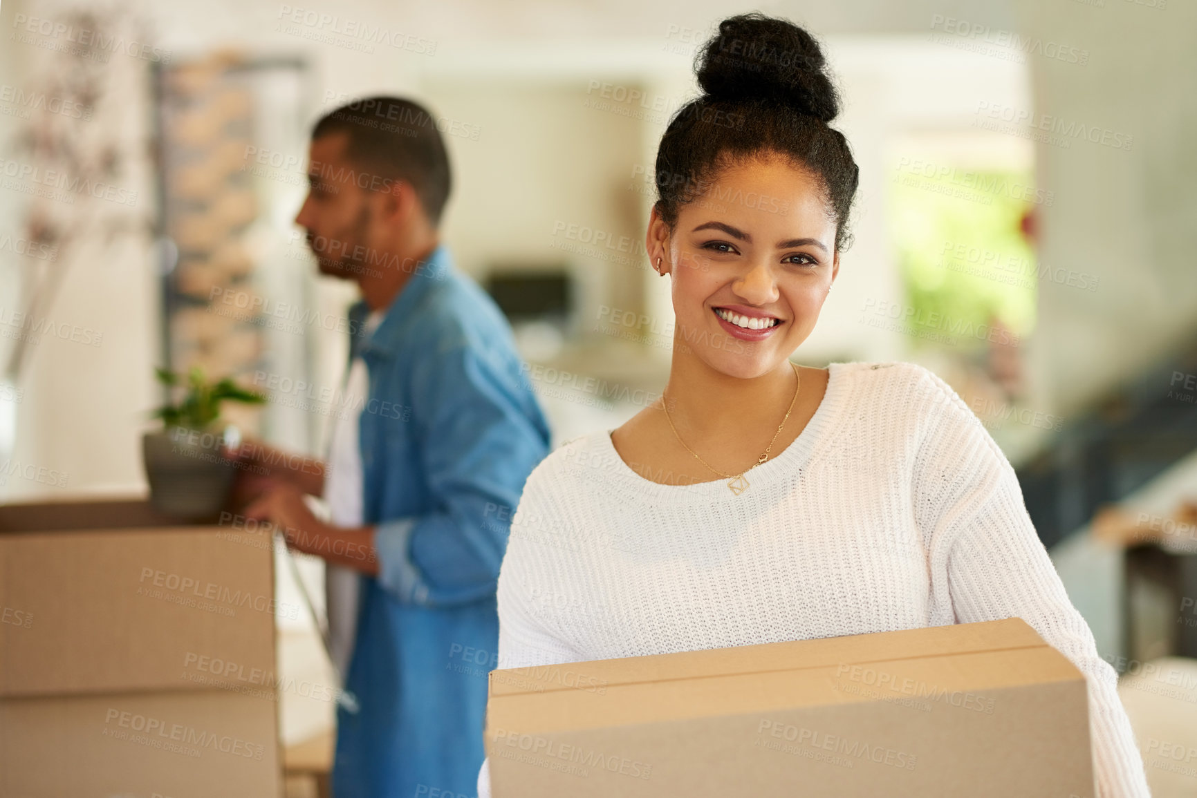 Buy stock photo Shot of a happy young woman carrying cardboard boxes into her new home with her boyfriend