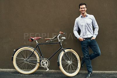 Buy stock photo Portrait of a young man posing with his bicycle against a dark wall