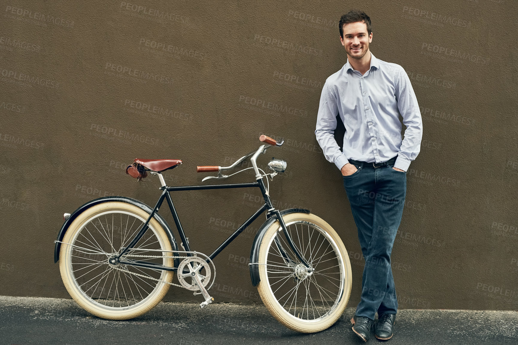 Buy stock photo Portrait of a young man posing with his bicycle against a dark wall