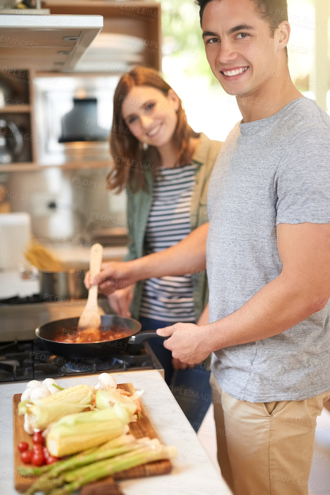 Buy stock photo Portrait of a happy young couple cooking a meal together in their kitchen