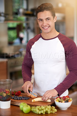 Buy stock photo Portrait of a happy young man preparing a healthy breakfast of fruit in his kitchen at home