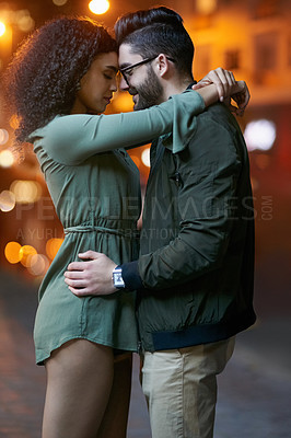 Buy stock photo Shot of a happy young couple embracing outdoors at night