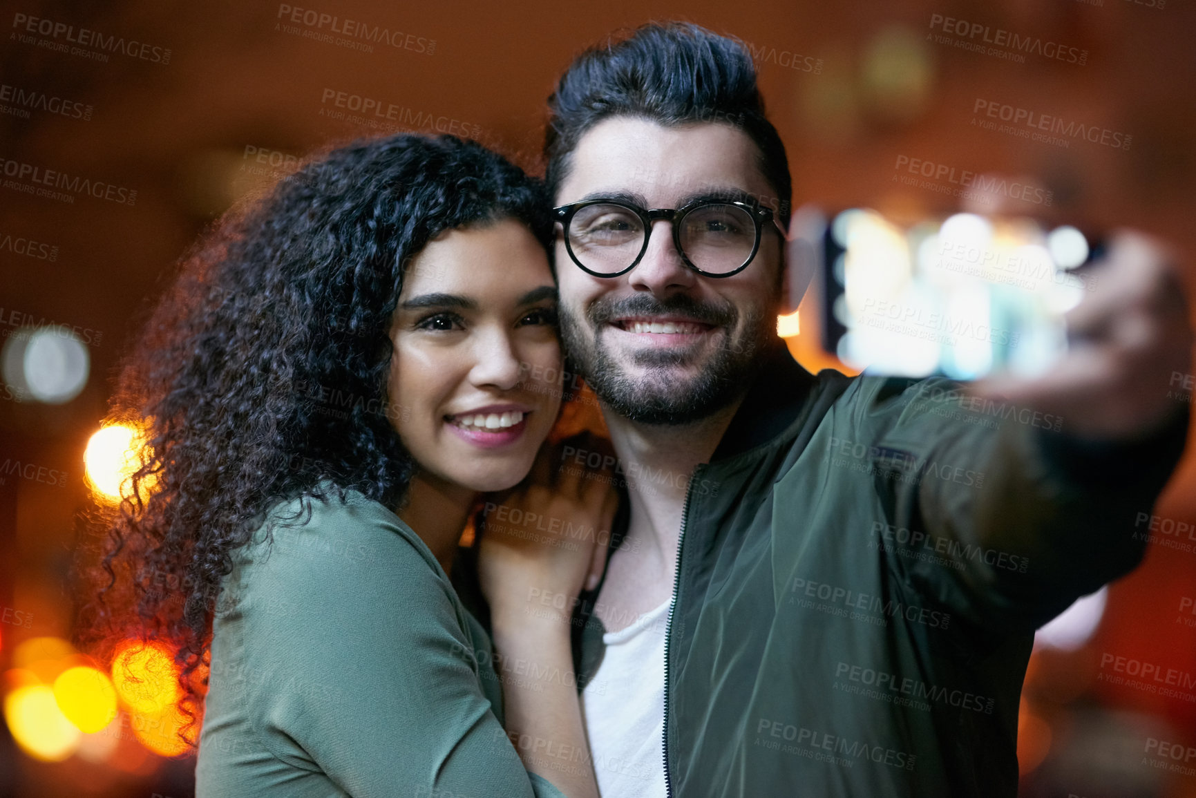 Buy stock photo Shot of a happy young couple taking a selfie outdoors at night